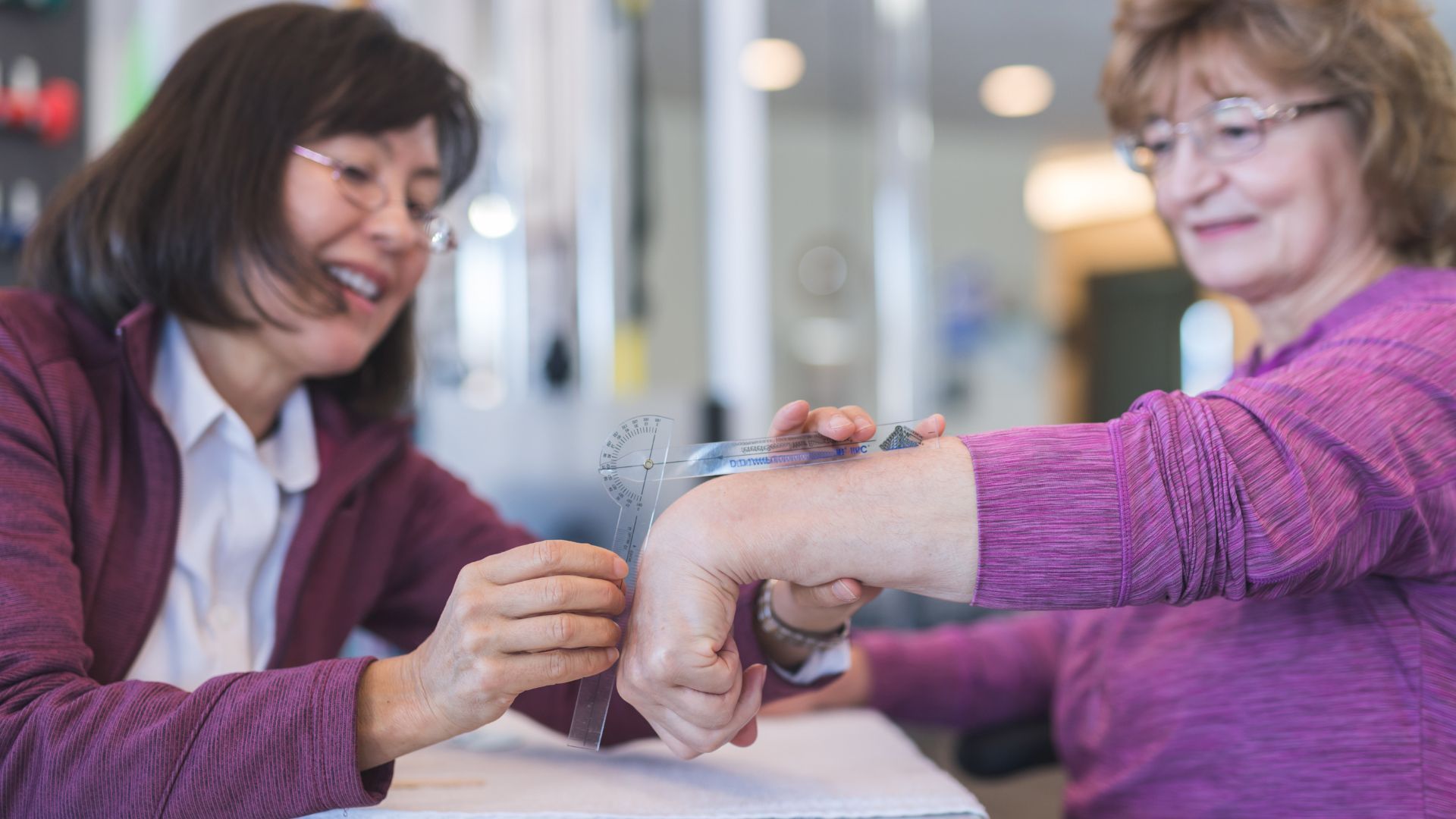 Therapist using a goniometer on a patient's wrist in a clinic.
