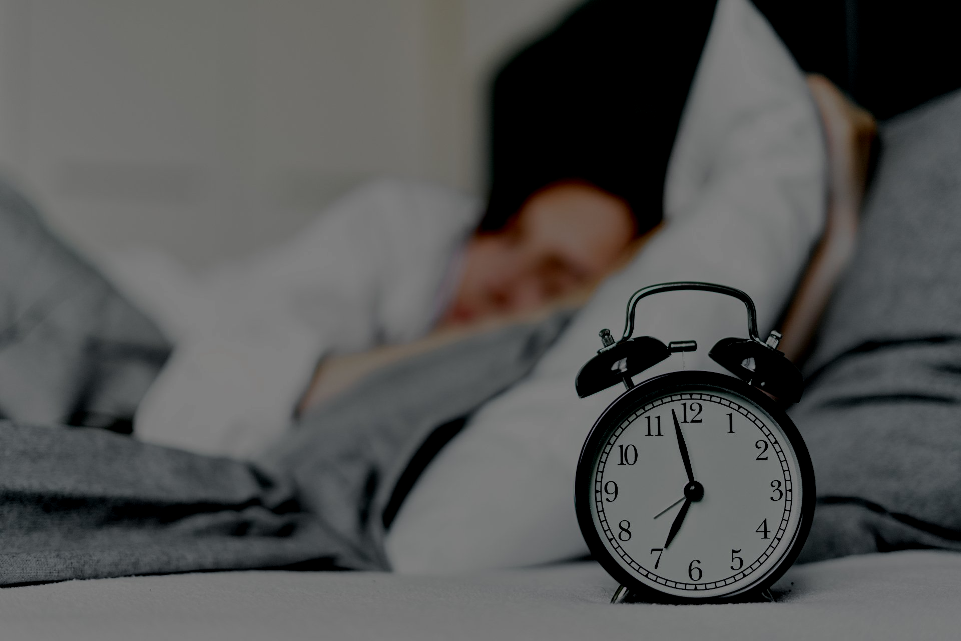 Alarm clock next to someone sleeping, representing time or rest.