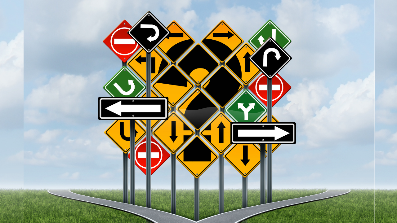 Multiple colorful road signs with directional arrows converge at a pathway fork, symbolizing the many directions and decisions along the autoinflammatory arthritis patient journey. The signs include red, yellow, black, and green markers against a cloudy sky and grassy landscape, representing patient support's different resources and paths.