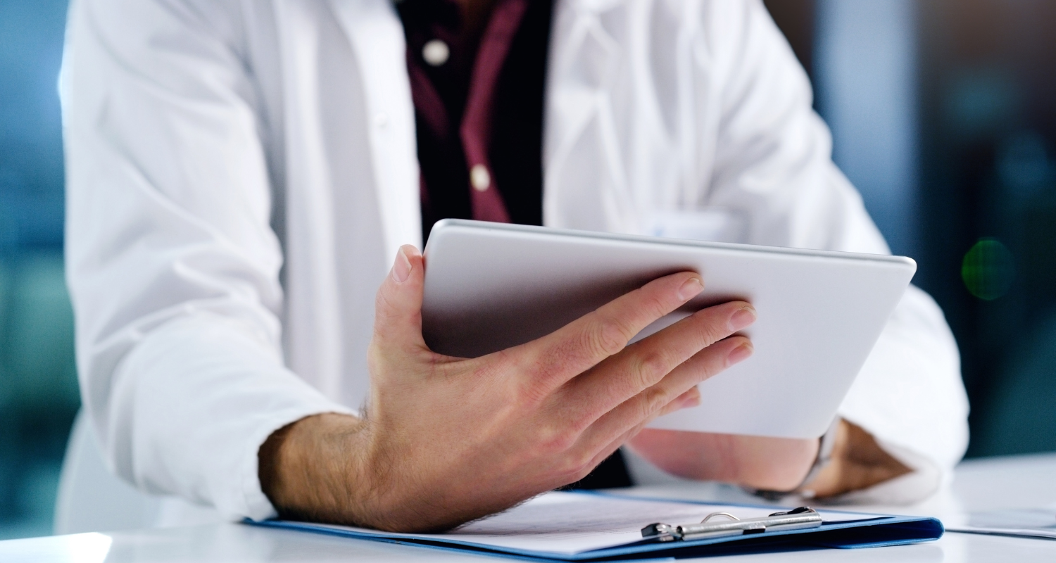 Person in a white coat holding a tablet at a desk in an office setting