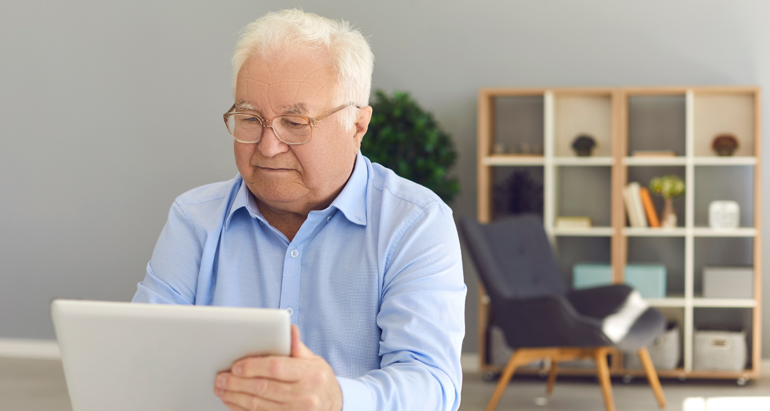 Older man using a tablet at a desk in a bright home office