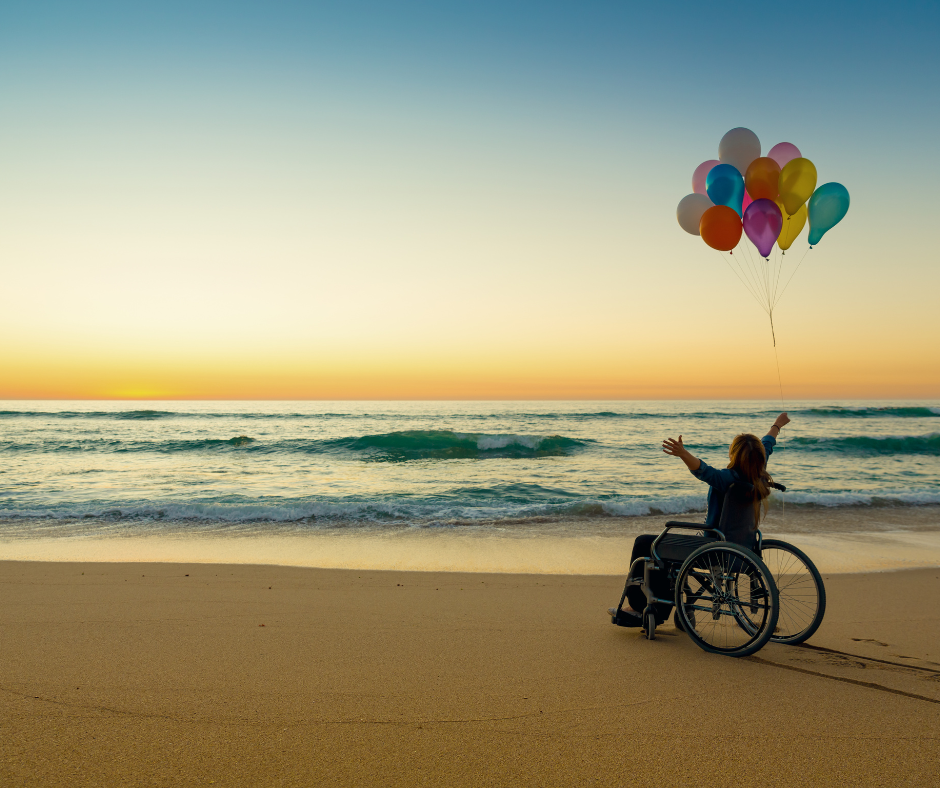 Woman in wheelchair with balloons excited to be on a beach during sunset