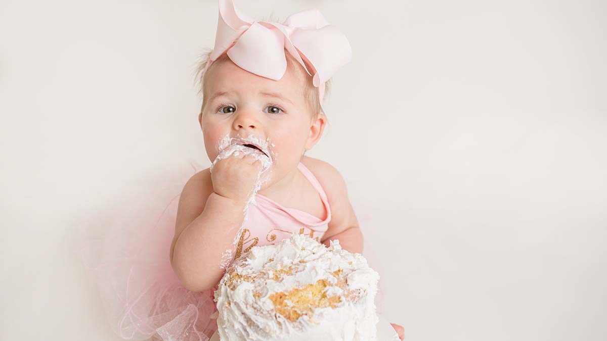 A baby girl in a pink dress is eating a cake.
