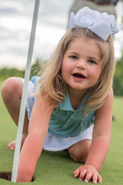 A little girl wearing a white bow is crawling on a golf course