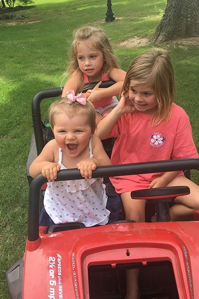 three young girls smiling and driving a mini jeep