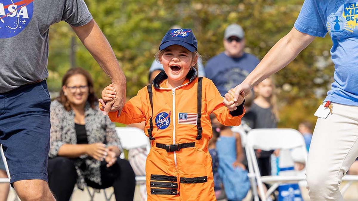 A little girl in an astronaut costume is holding hands with her parents.