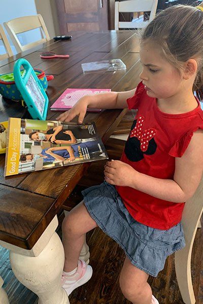 a young girl sitting at a desk looking at a magazine