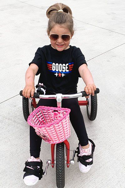 A little girl wearing a goose shirt is riding a tricycle