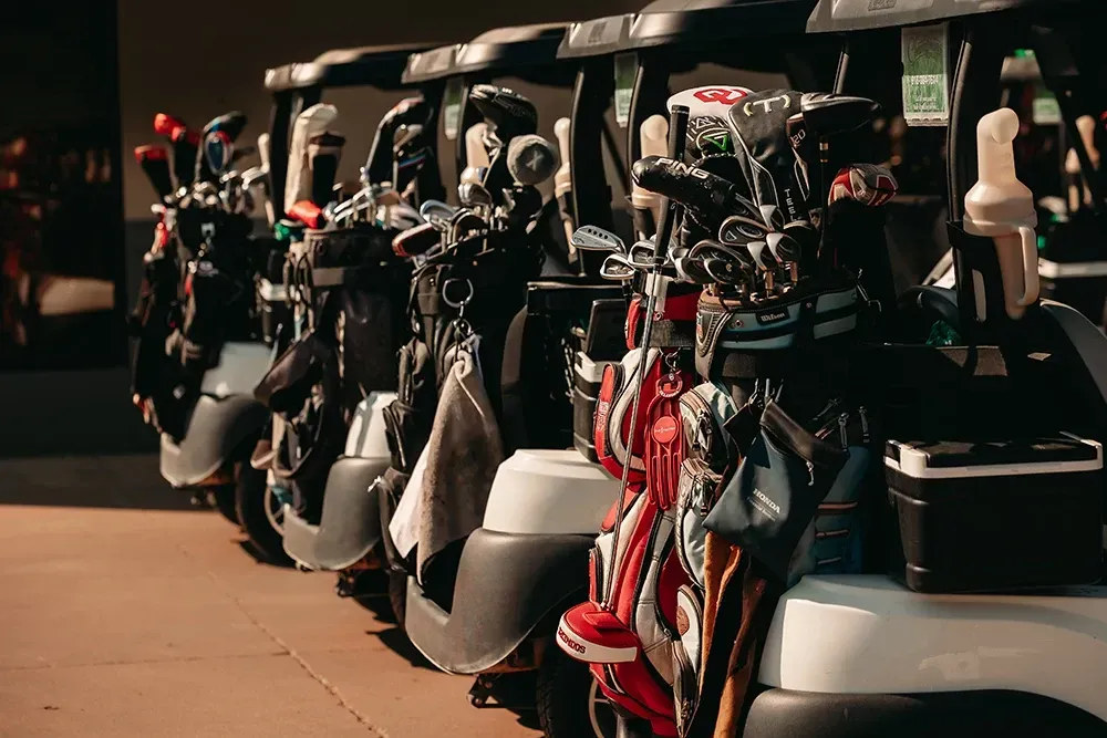 A row of golf carts filled with golf clubs and bags.