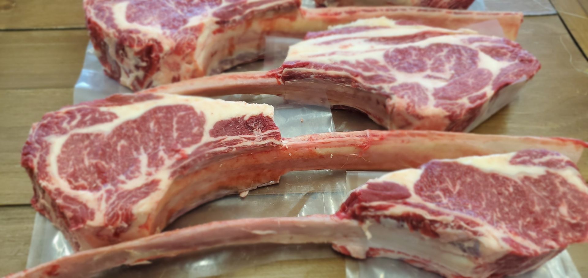 Three raw steaks with long bones are sitting on a wooden table.