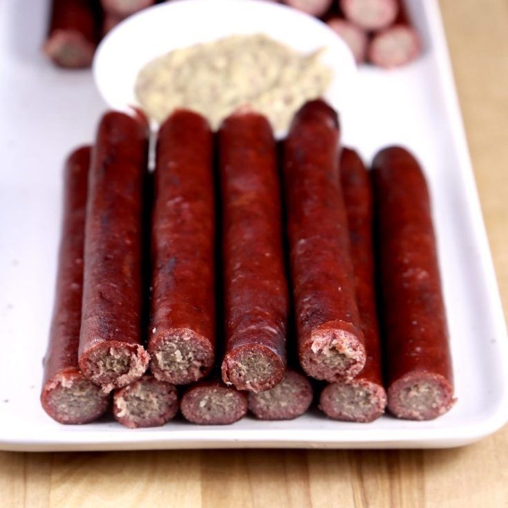 A tray of sausage sticks with a bowl of mustard