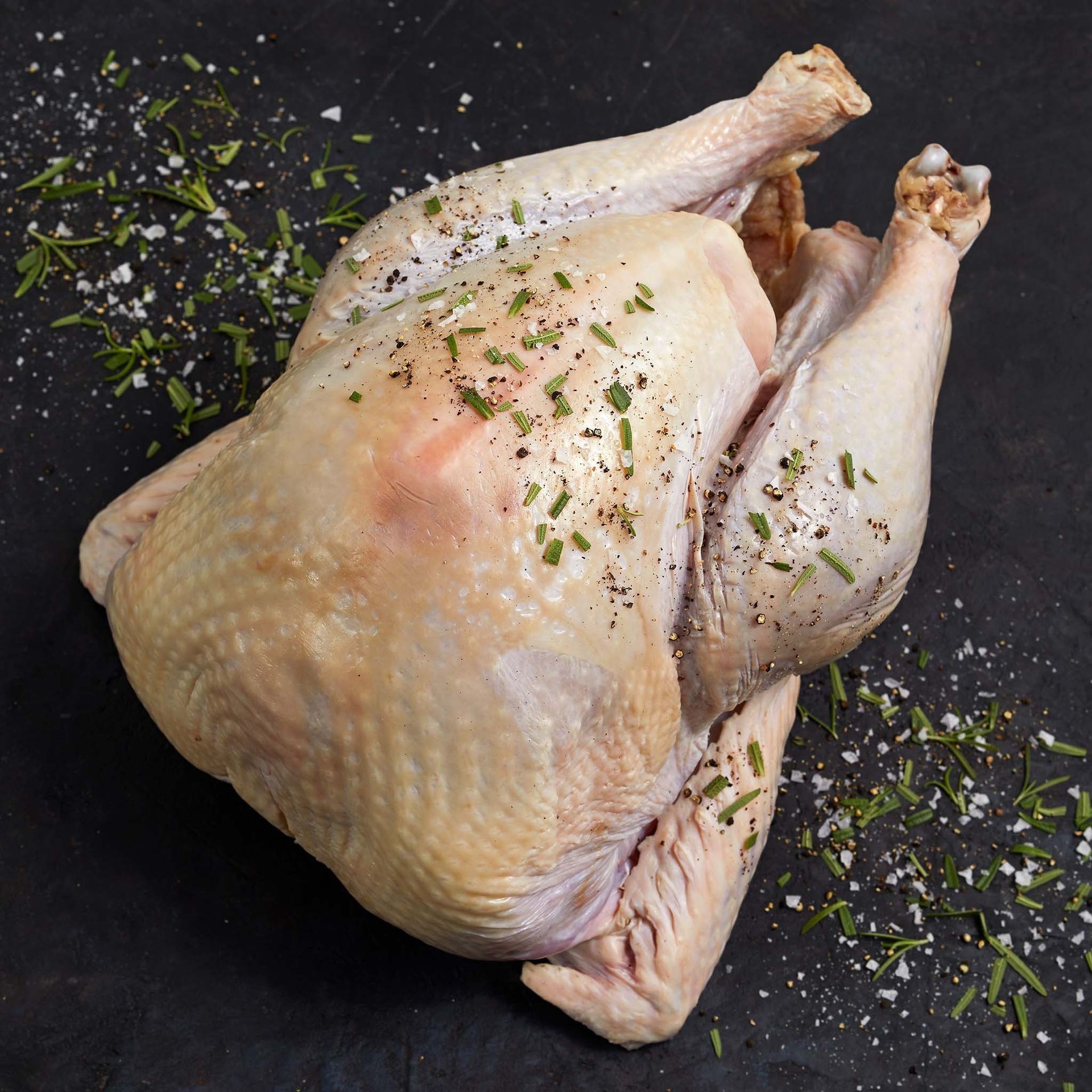 A whole chicken is sitting on a table with salt and pepper on it.