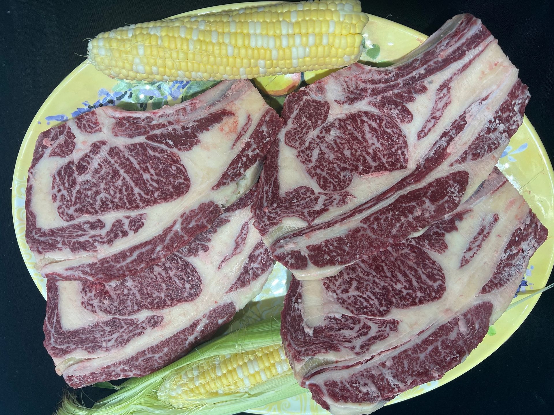 Two steaks are sitting on a plate next to corn on the cob.