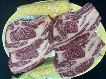 Two steaks are sitting on a plate next to corn on the cob.