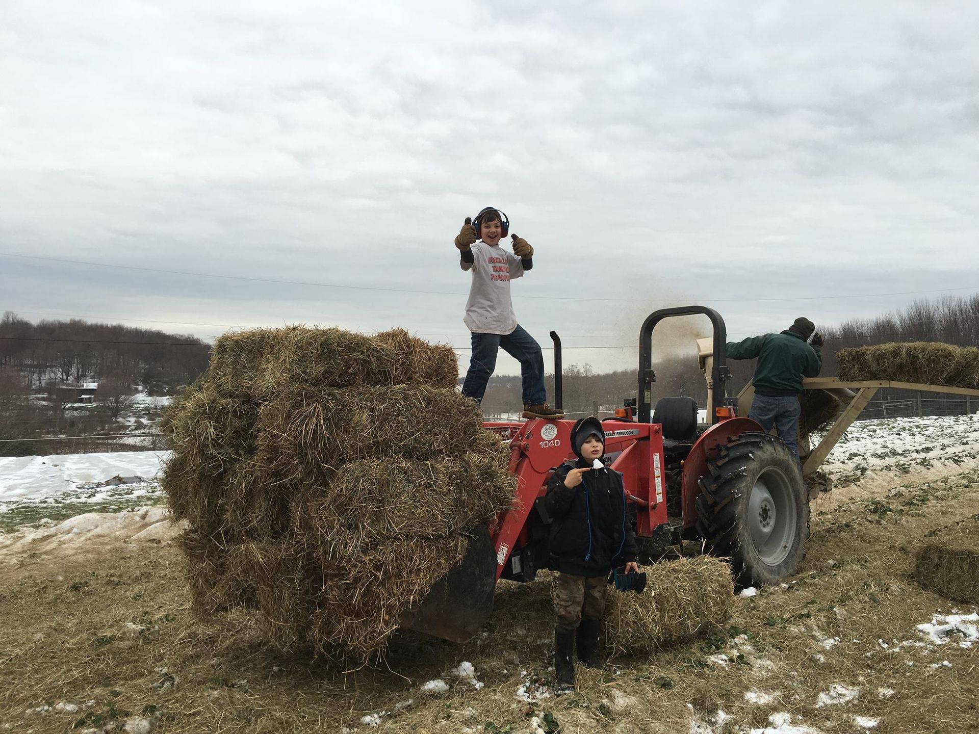 Two children are standing on top of a tractor filled with hay.
