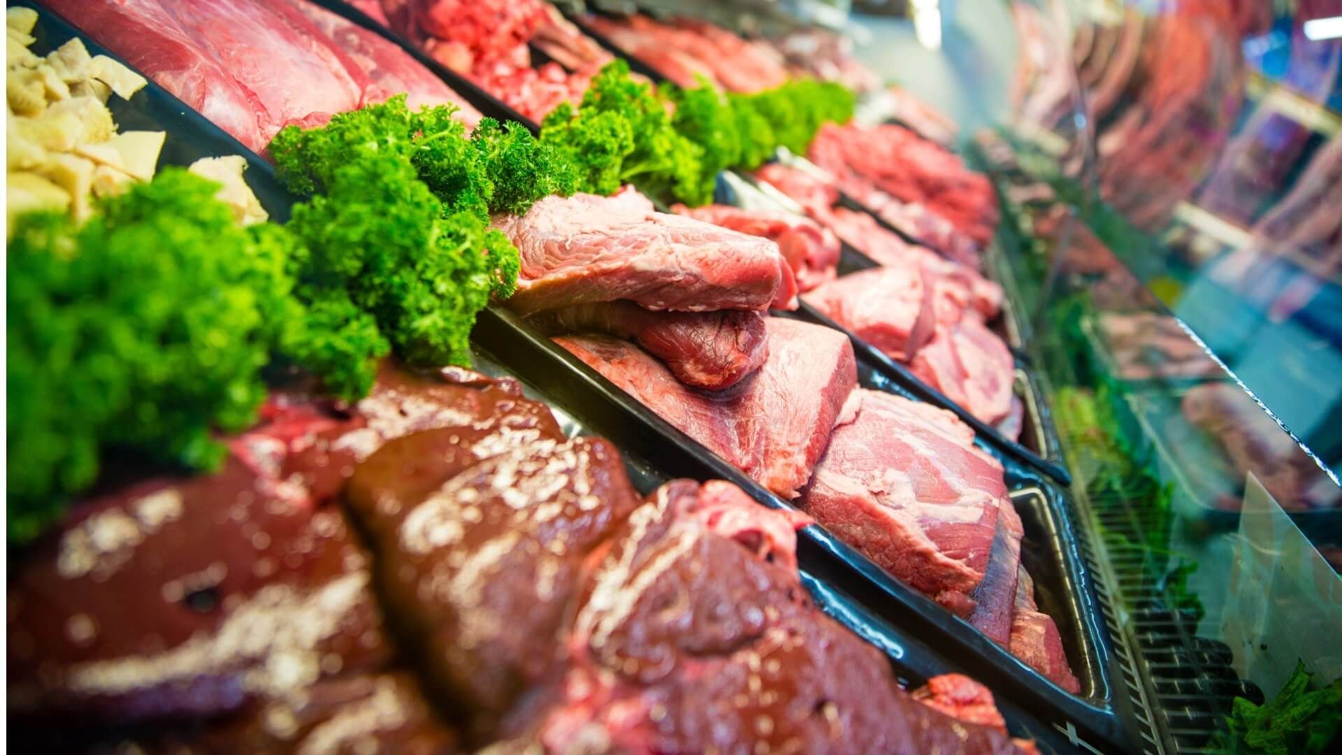 A variety of meats and vegetables are displayed in a butcher shop.