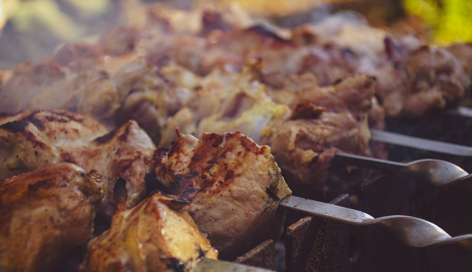 A close up of meat being cooked on skewers on a grill.