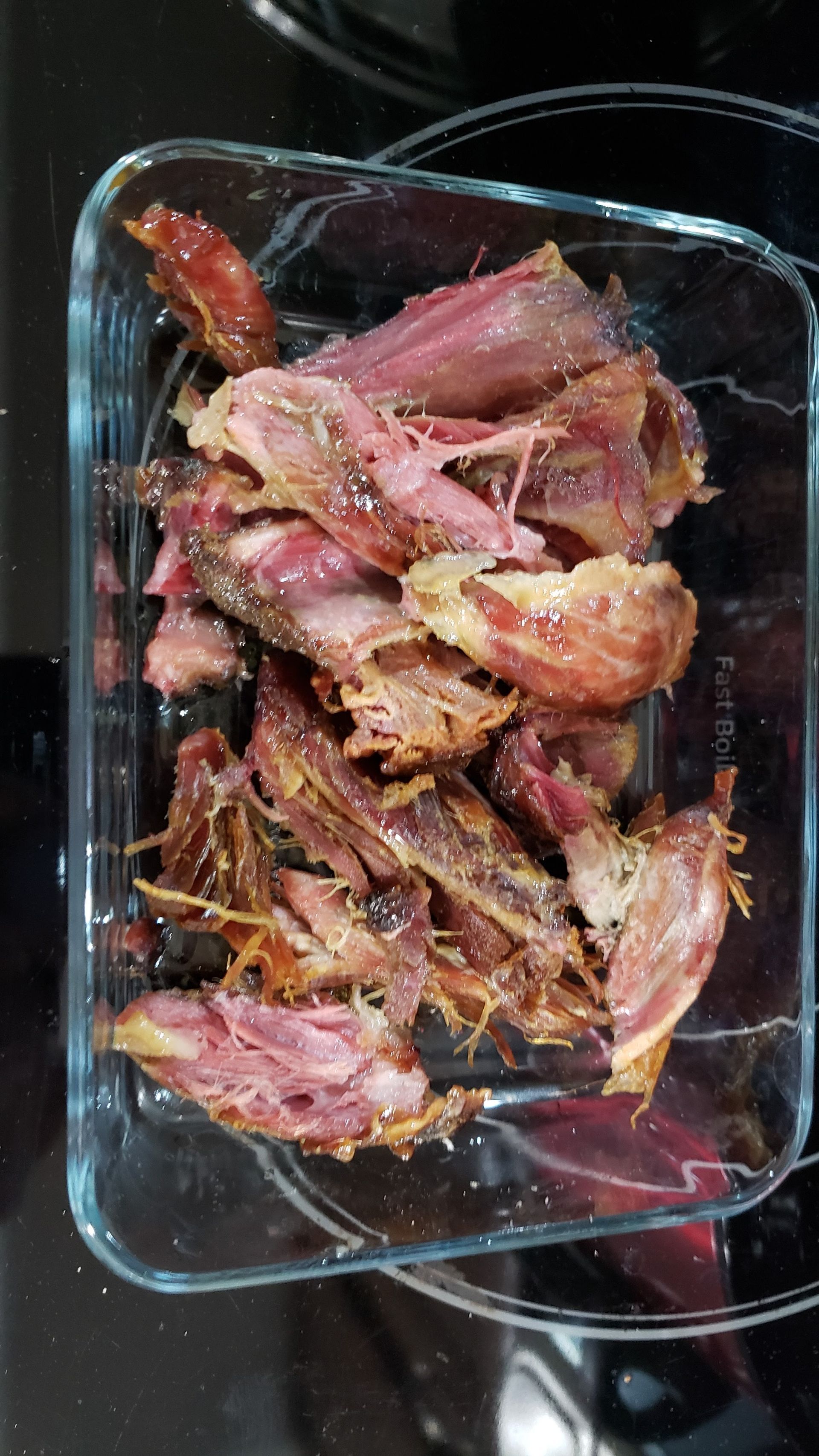 A glass container filled with chopped meat is sitting on top of a stove.