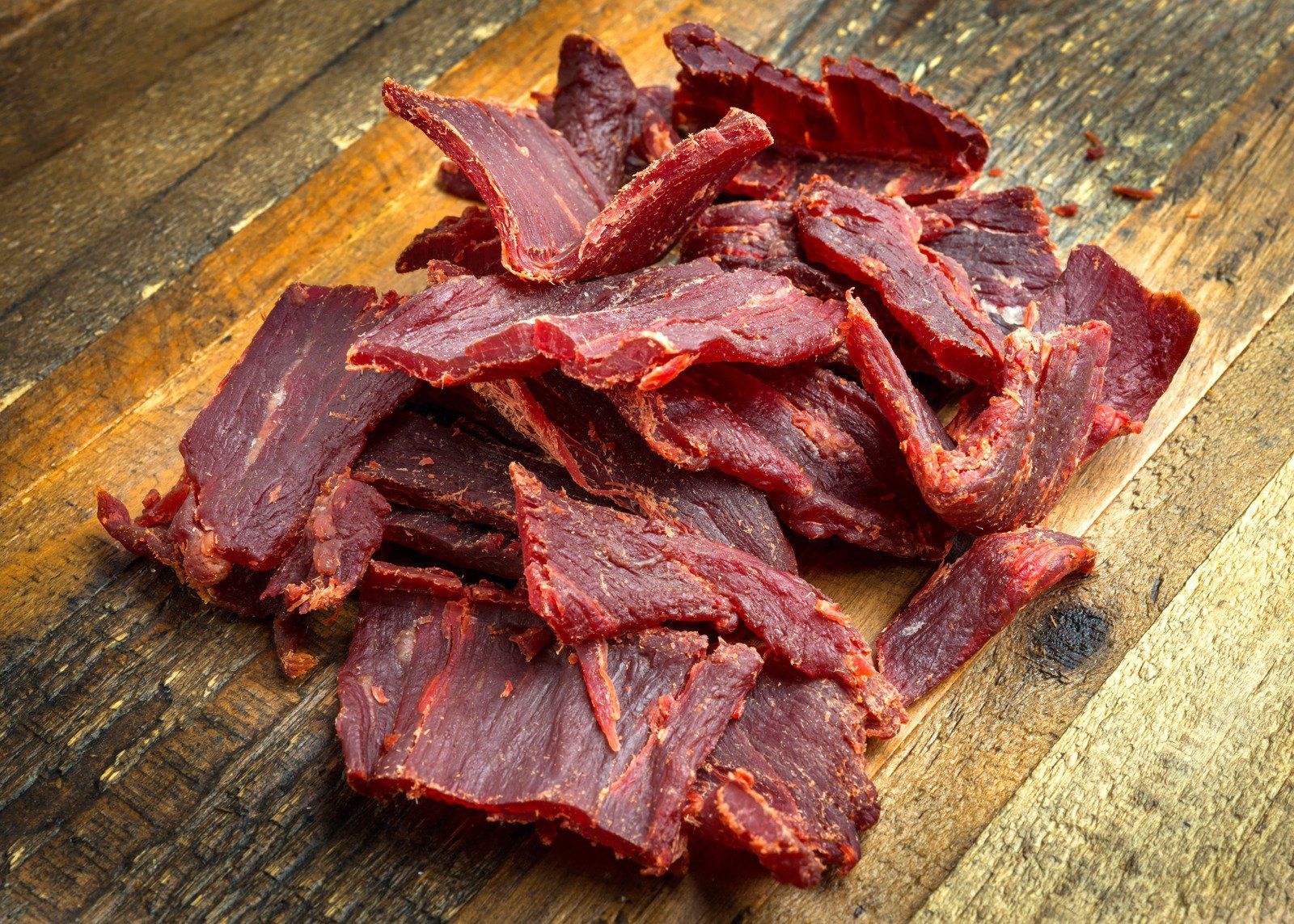 A pile of beef jerky is sitting on a wooden cutting board.