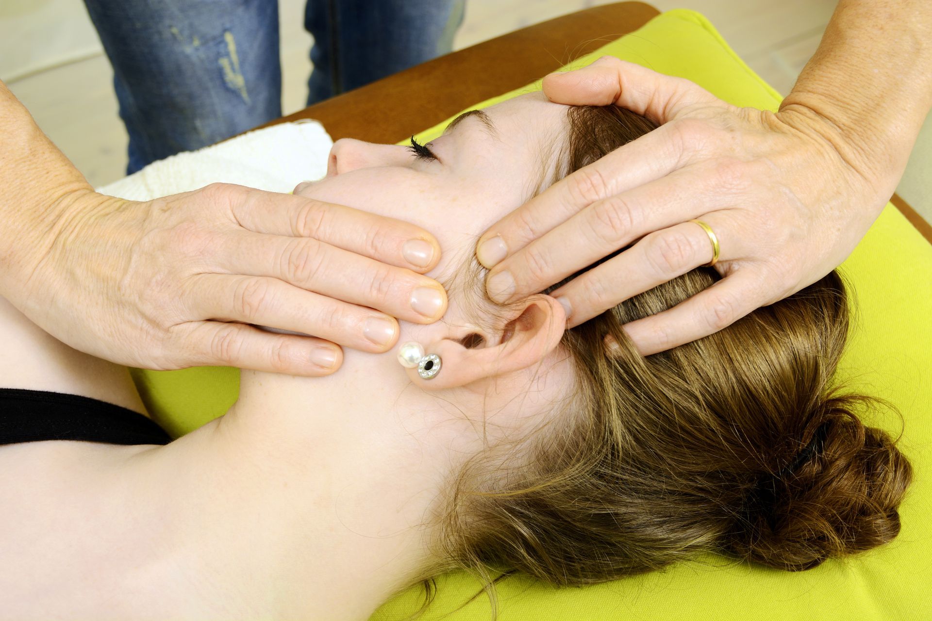Chiropractor performs a gentle jaw adjustment on a patient lying on a treatment table.