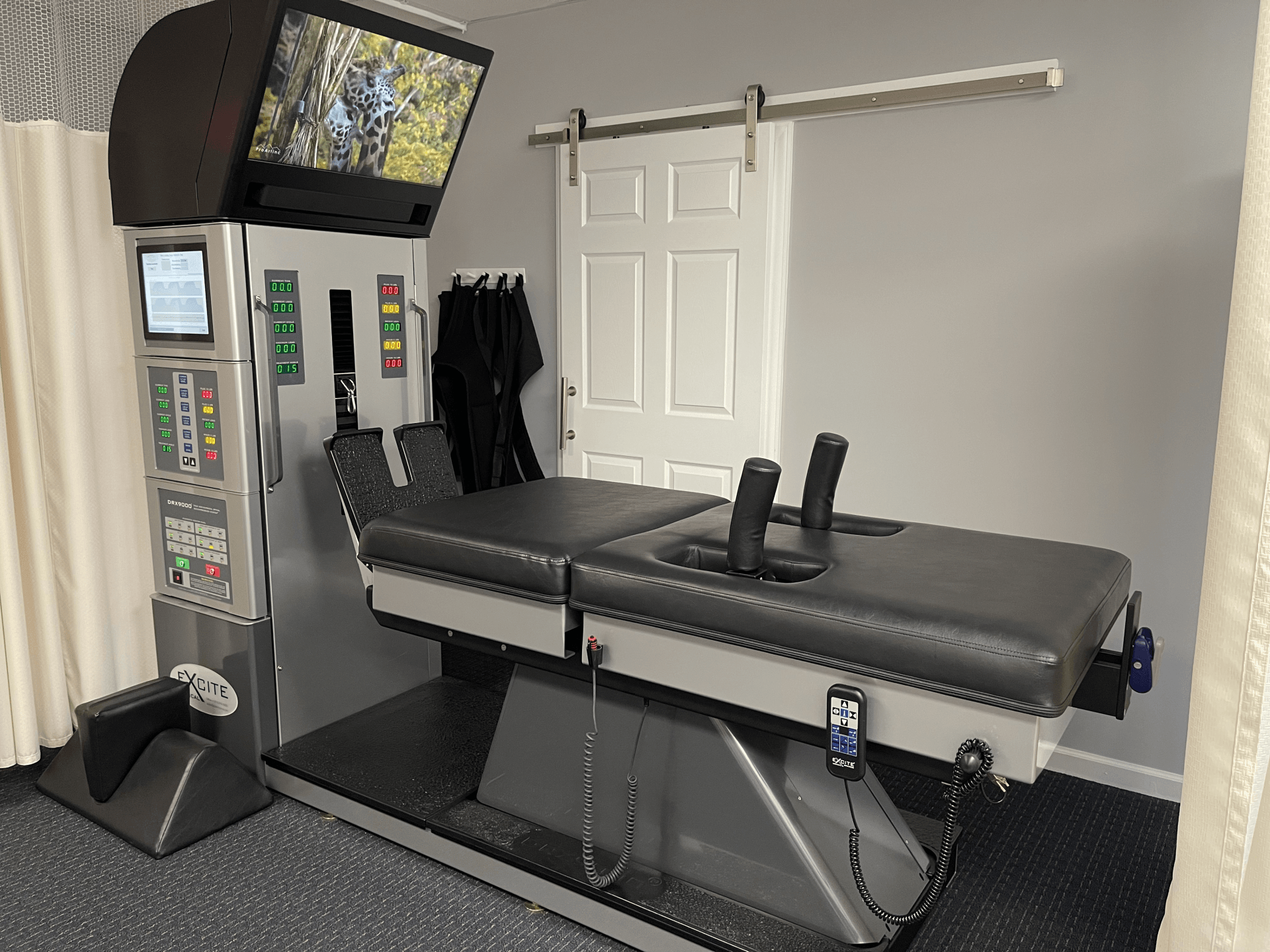 Chiropractic decompression table with a video screen in a light gray room.