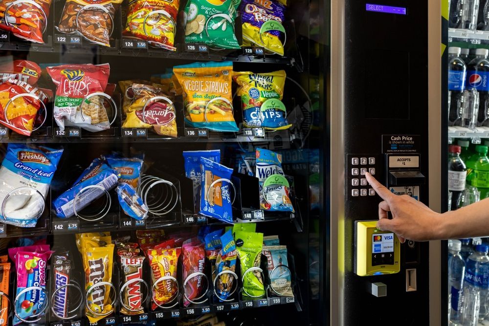 Hand selecting a snack from a vending machine filled with chips, cookies, and candy.
