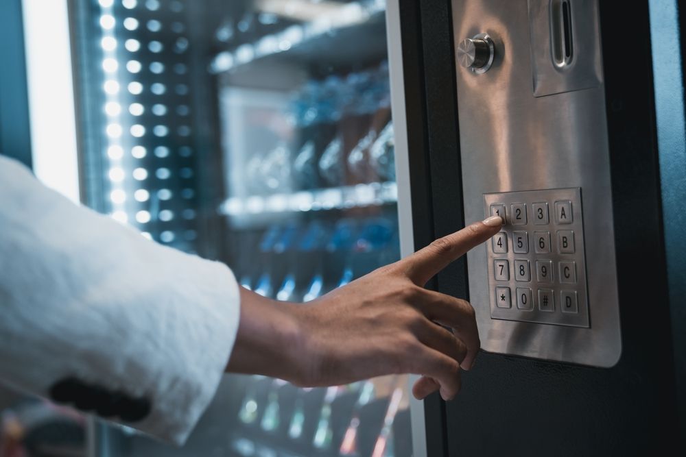 Person's hand pressing a number on a vending machine keypad. Blue and silver tones.