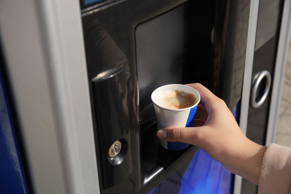 Hand holding a paper cup of coffee from a vending machine.