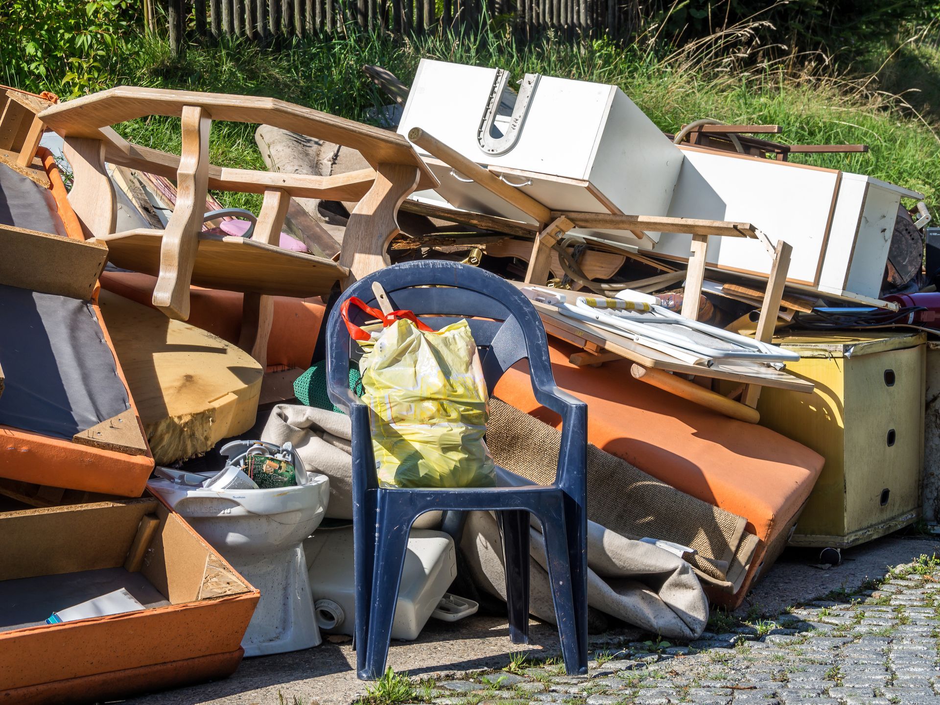Pile of discarded furniture and debris outdoors, including a blue plastic chair.