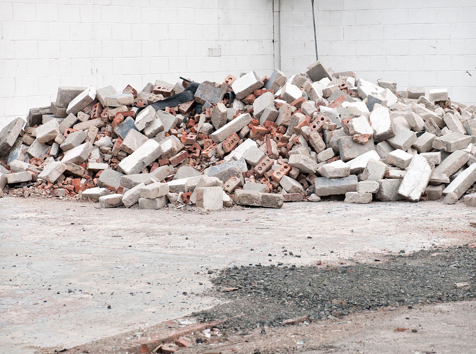 Pile of broken bricks and rubble against a white brick wall on a concrete surface.