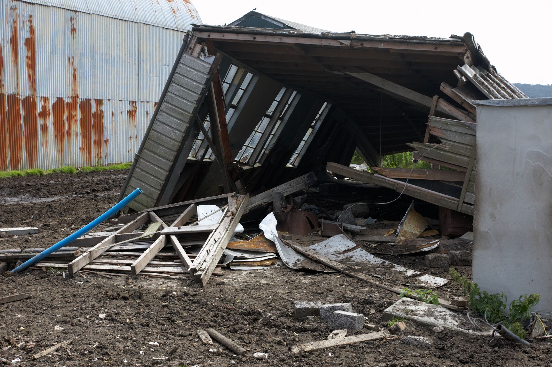 Collapsed wooden shed in muddy field, weathered and damaged.