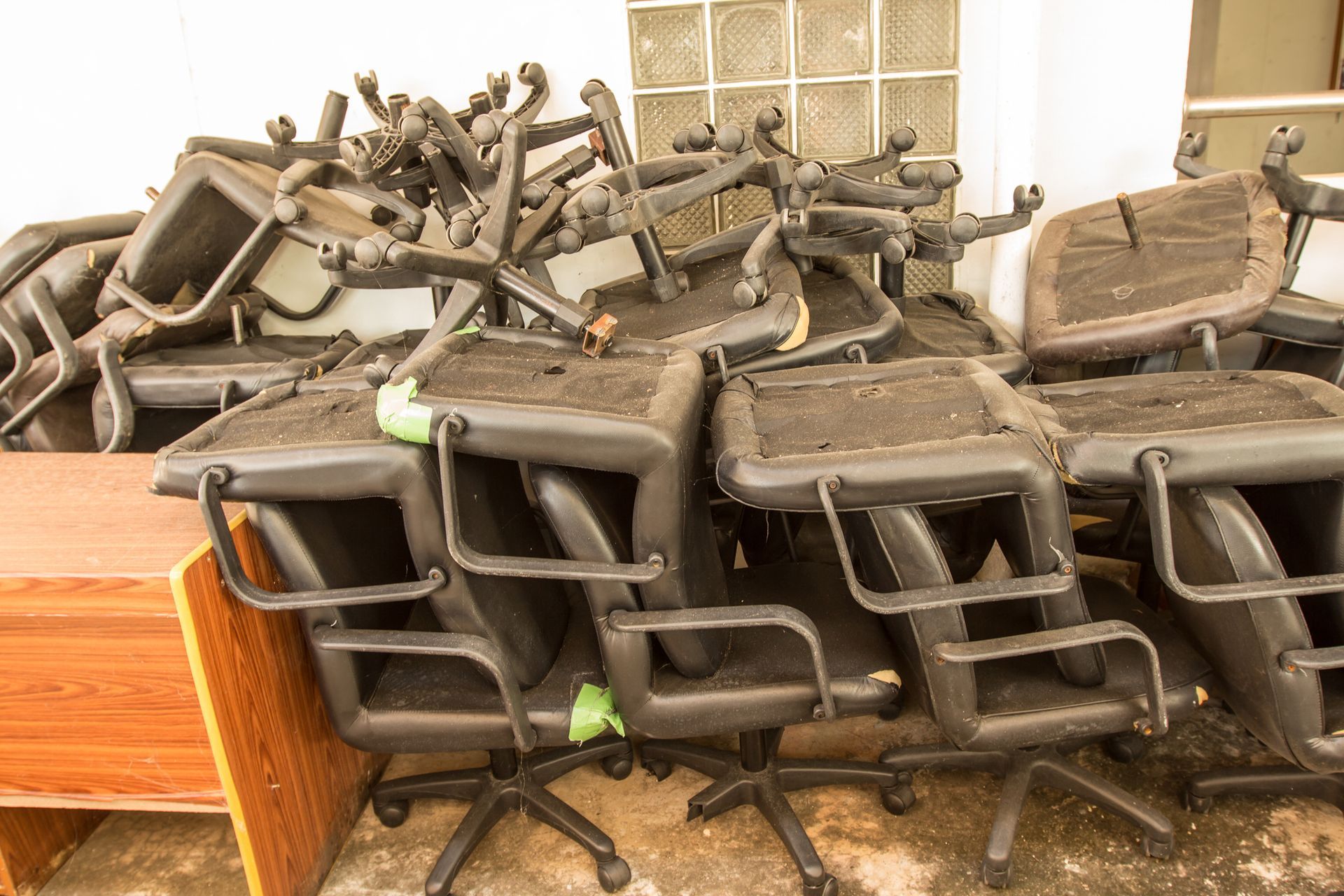 Pile of worn, black office chairs stacked against a wall.