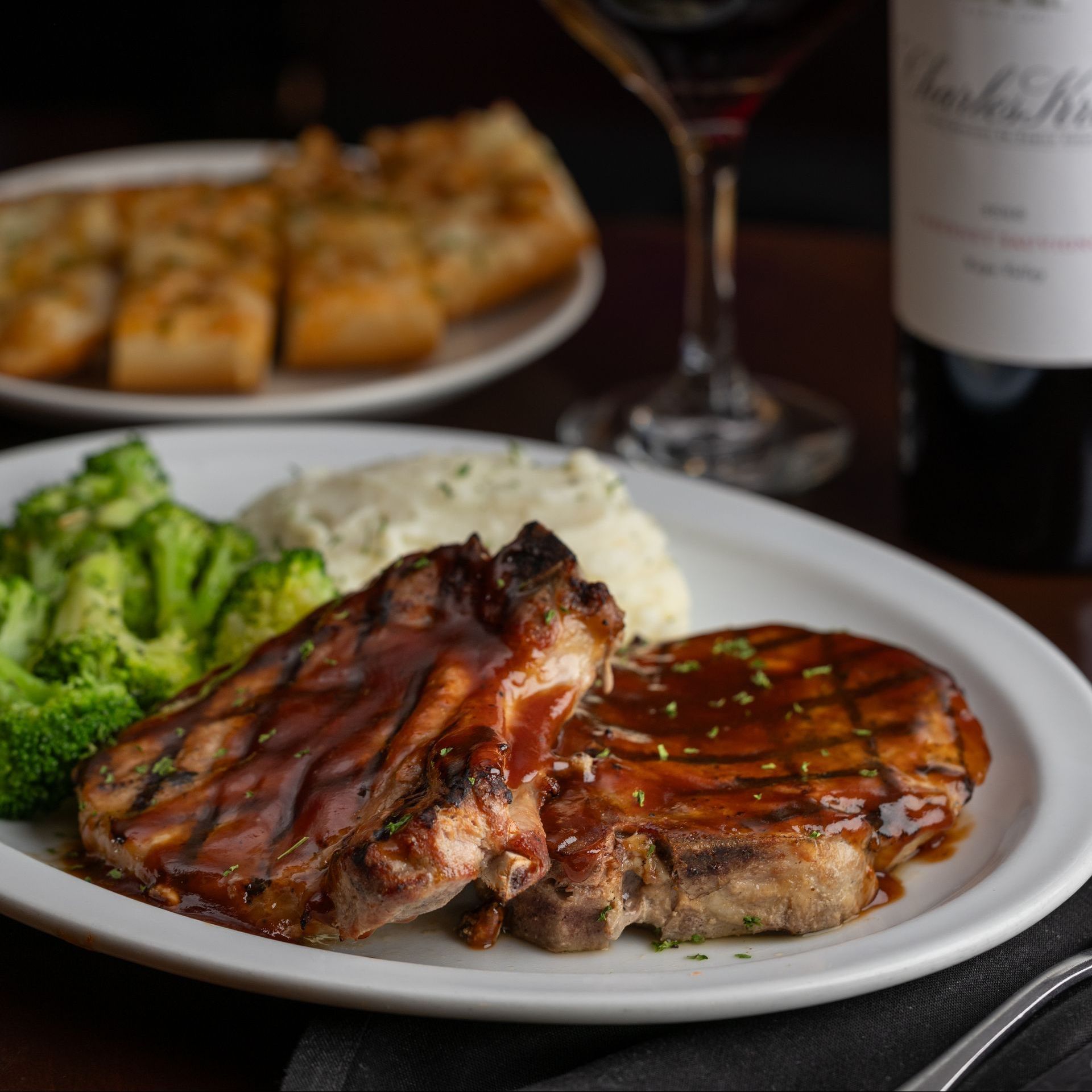 A white plate topped with steak and broccoli next to a bottle of wine at All That Jazz Dinner and Live Music