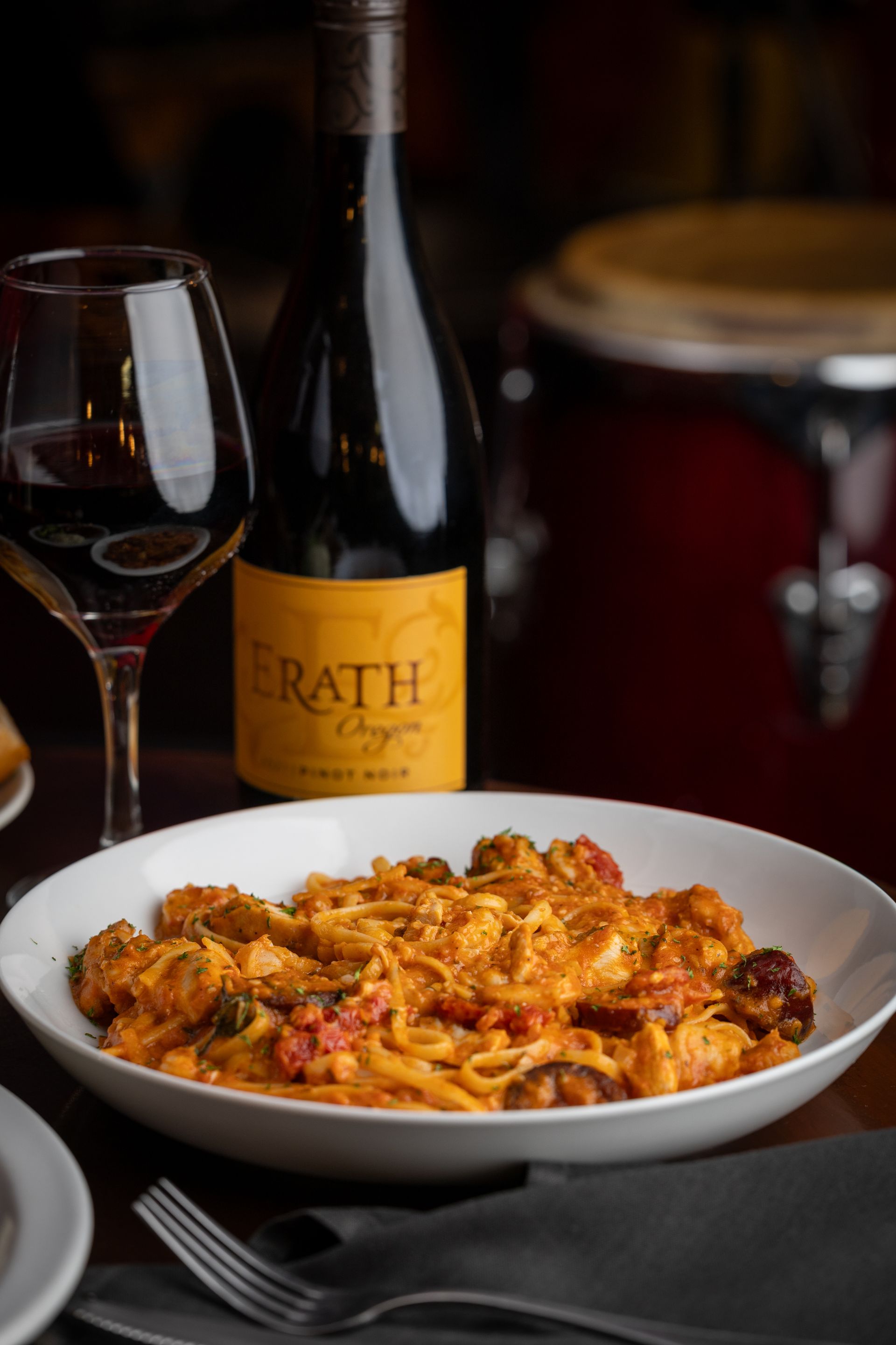 A plate of pasta next to a bottle and a glass of wine at All That Jazz Dinner and Live Music