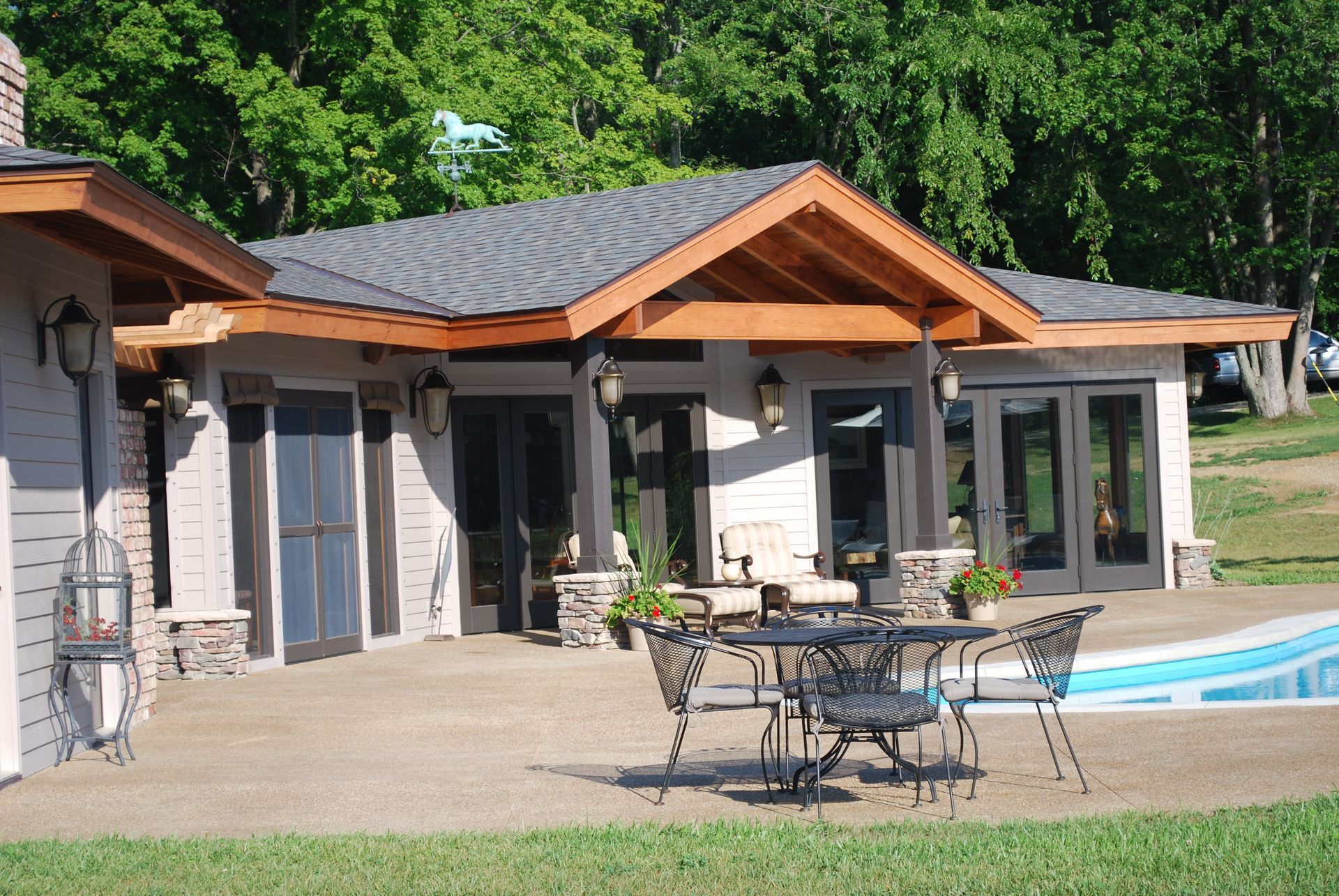 Beautiful, modern pool-house with a wooden roof, patio furniture, and a small pool in a green yard.