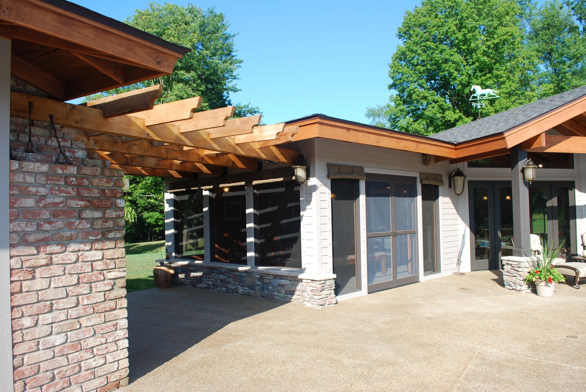 Modern pool-house exterior with a covered patio, wooden beams, and large glass doors under a sunny blue sky.