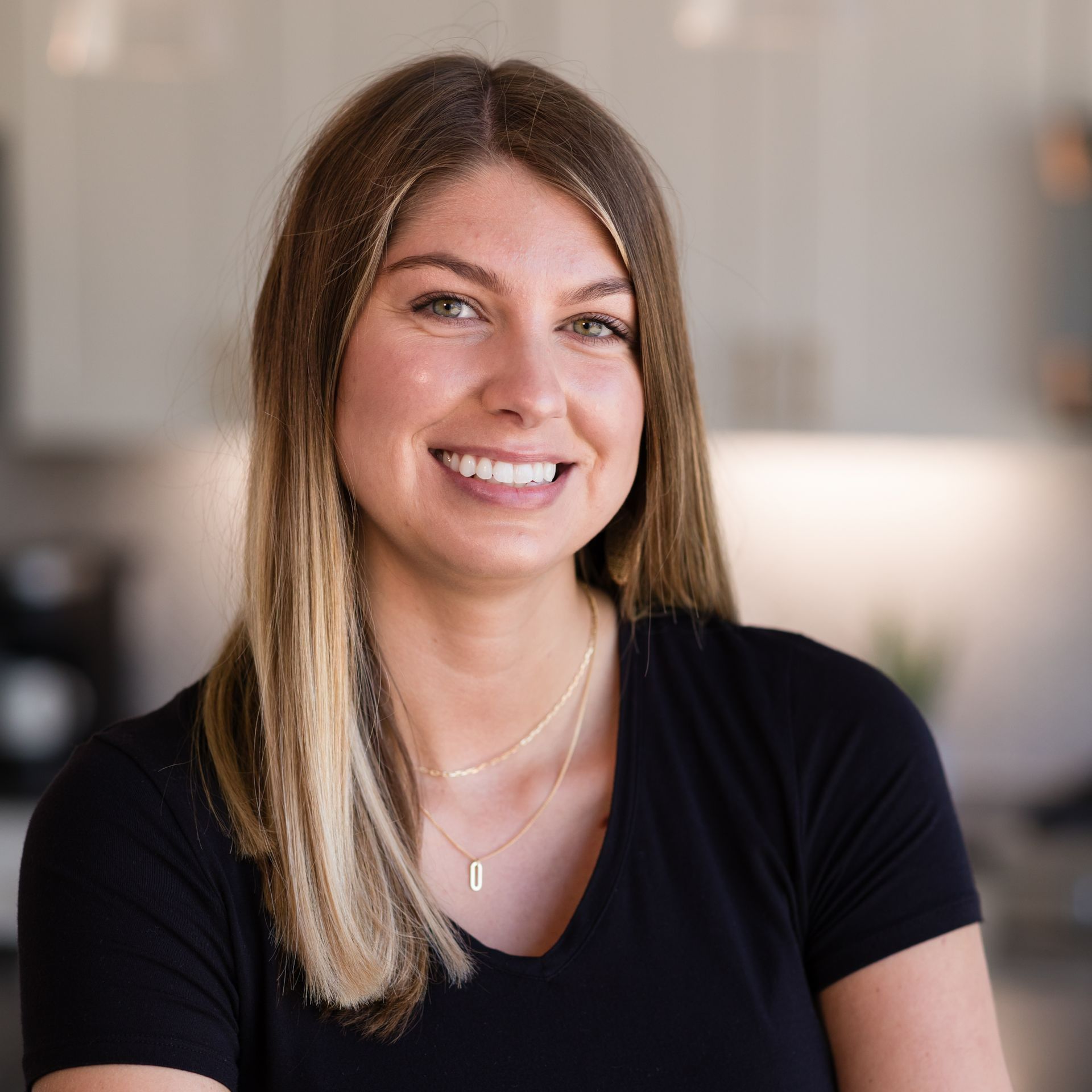 A woman wearing a black shirt and a necklace is smiling for the camera.