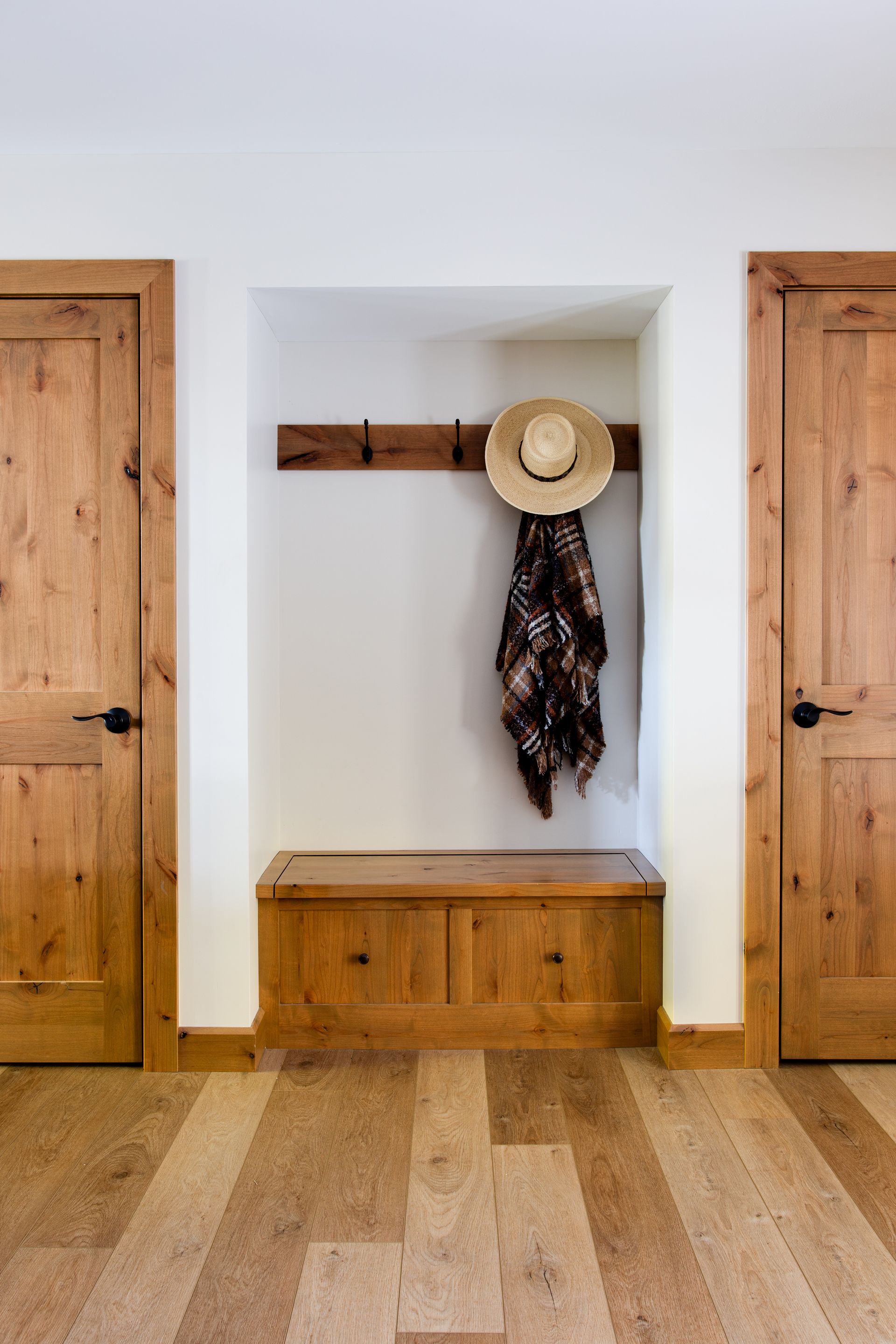 A hat and scarf are hanging on a wooden hook in a hallway.