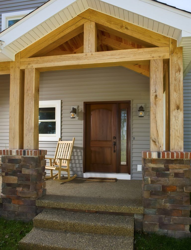 A rocking chair sits on the porch of a house with wooden beams. 
