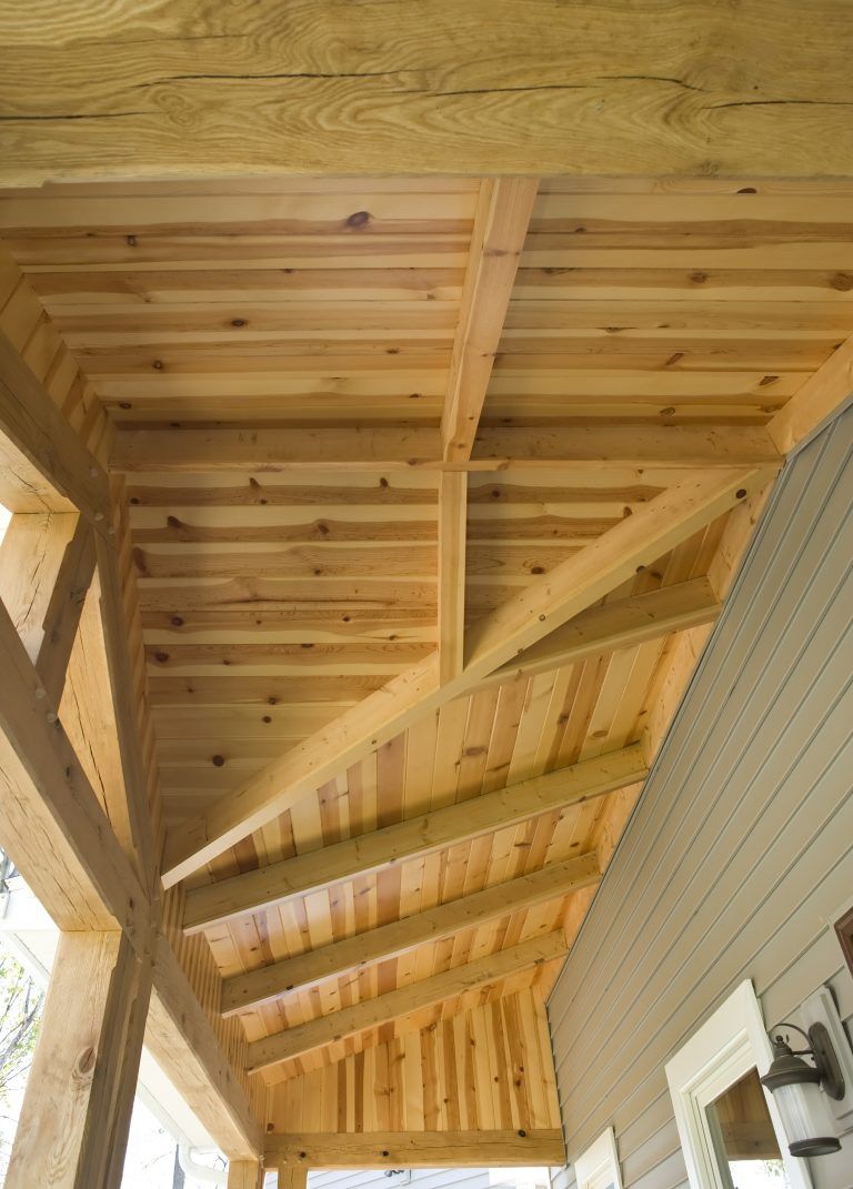 The ceiling of a wooden porch with a light on the side of the house.