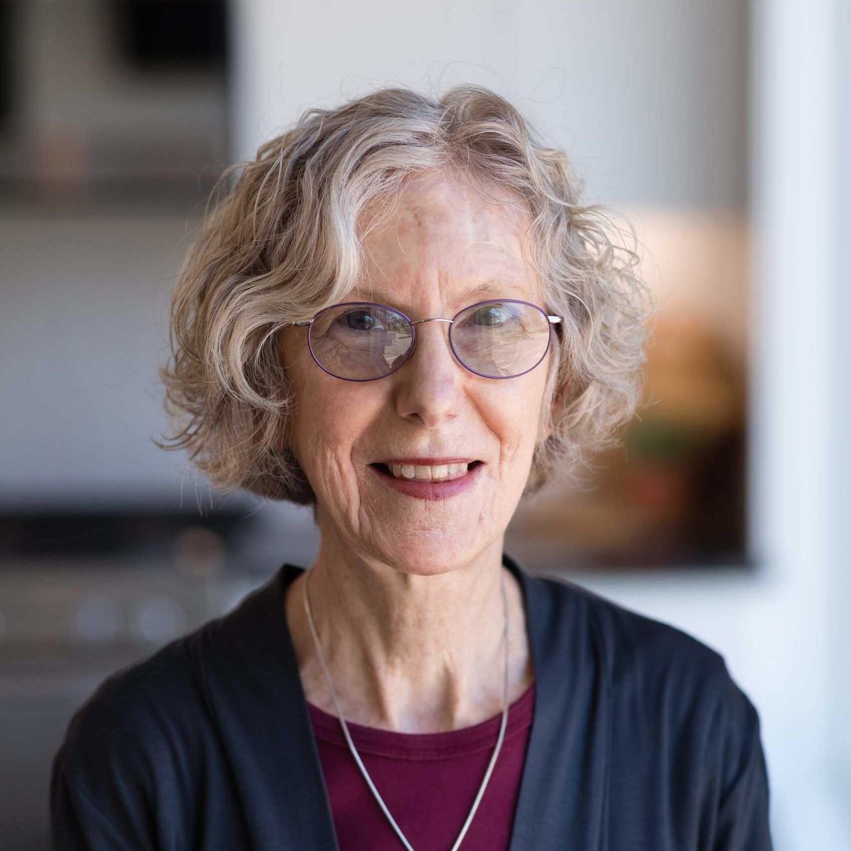 A woman wearing glasses and a necklace is smiling for the camera.