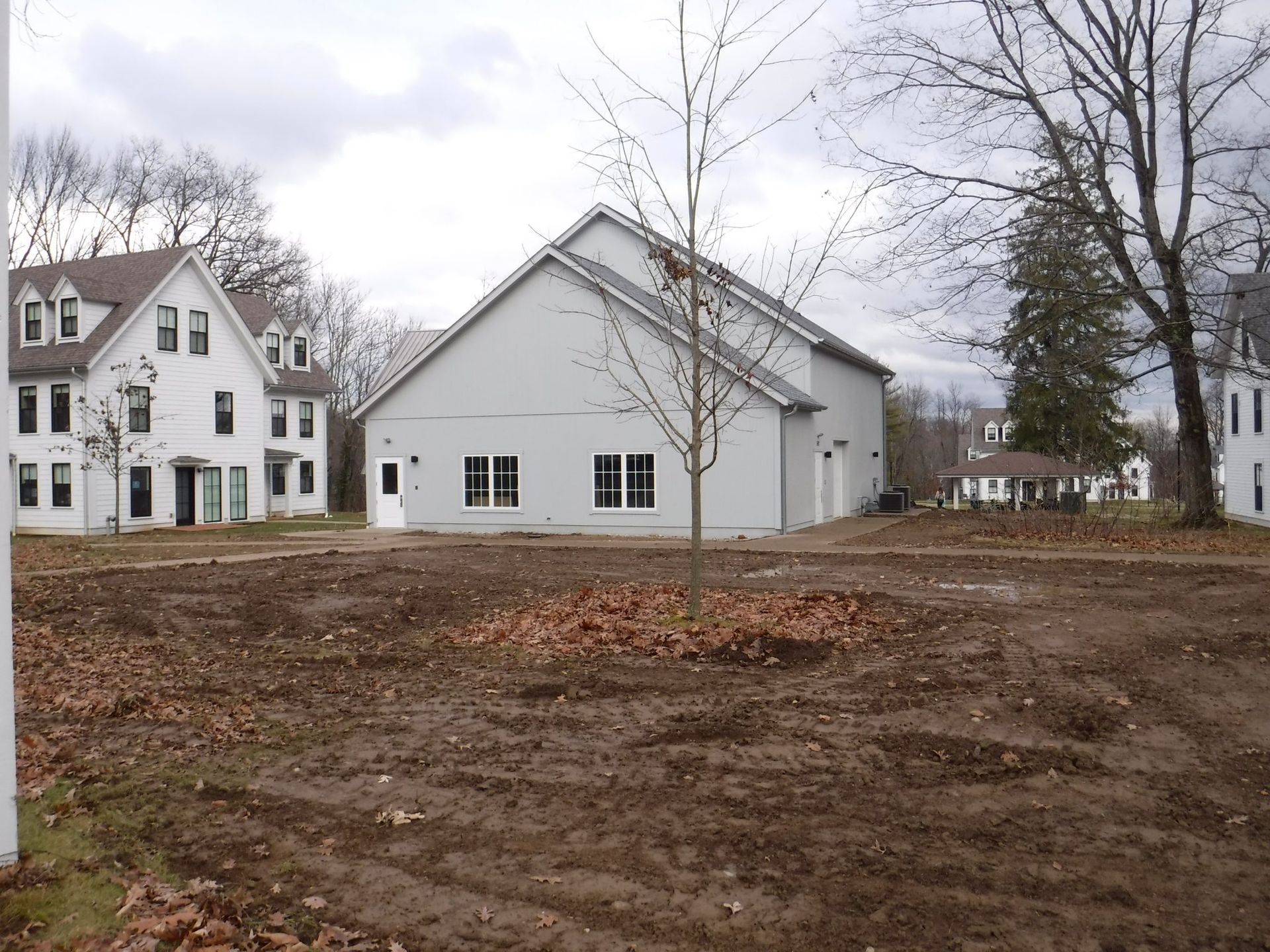 A white house with a brown roof sits in the middle of a dirt field.