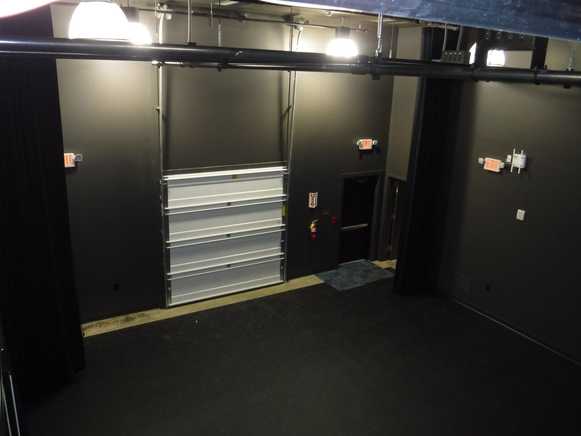 A dark room with a white door and a red exit sign.