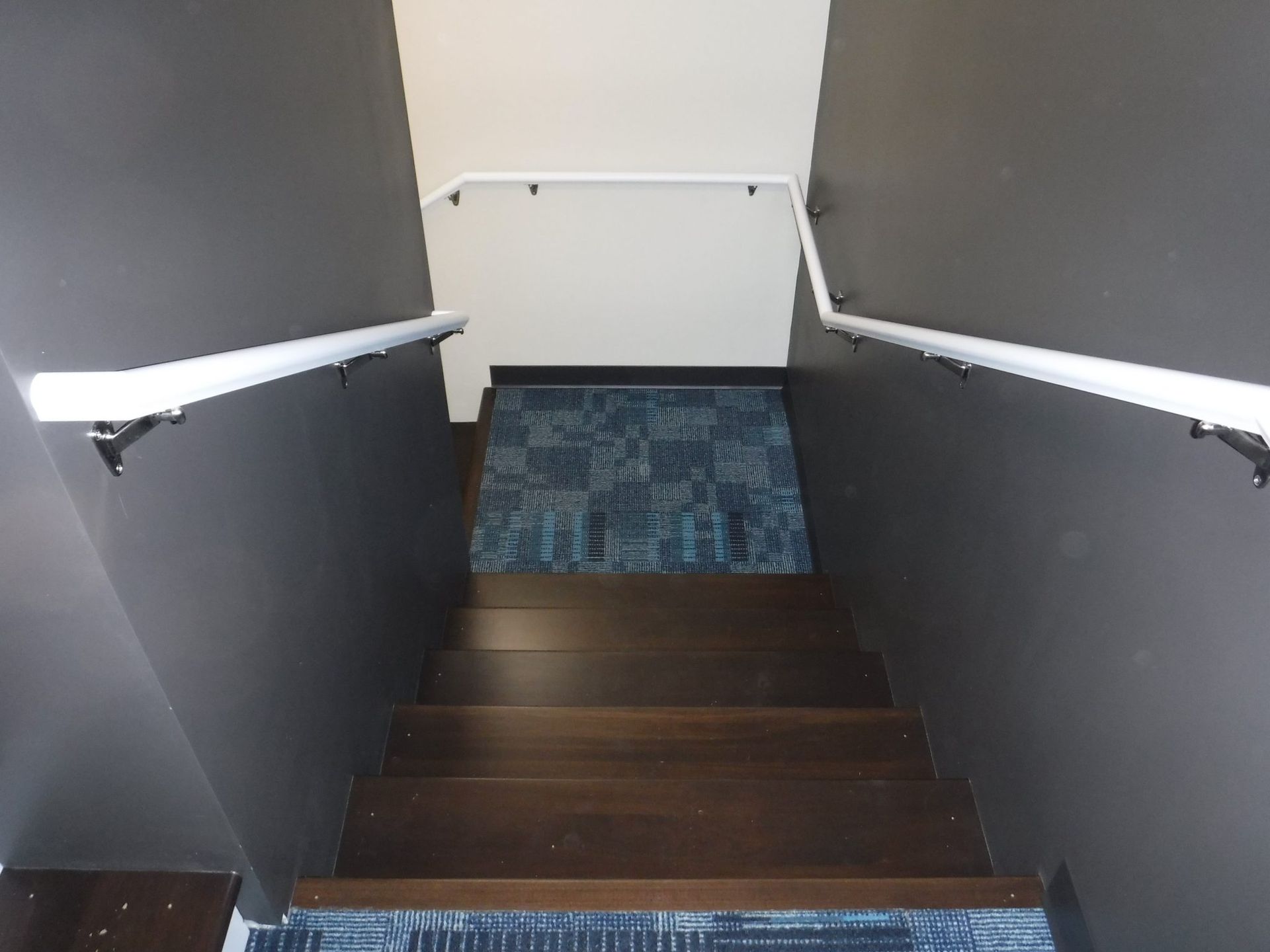 A staircase with a white railing and a blue rug on the floor.