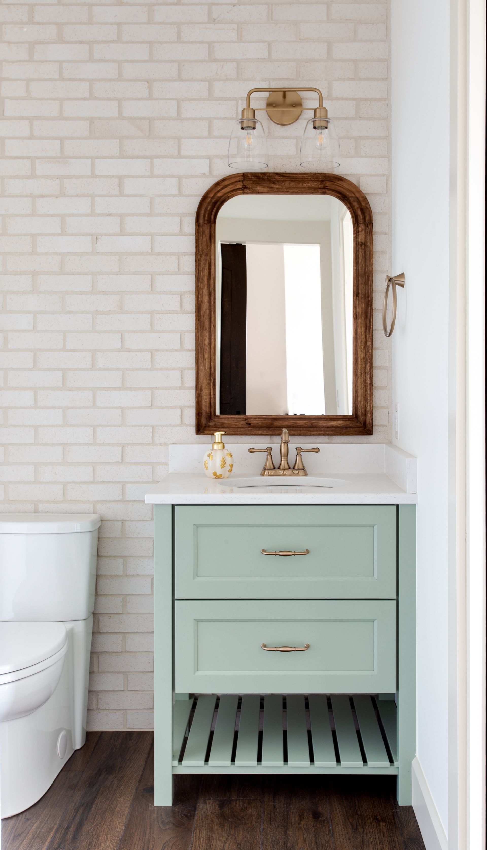 A bathroom with a sink, toilet, mirror and brick wall.