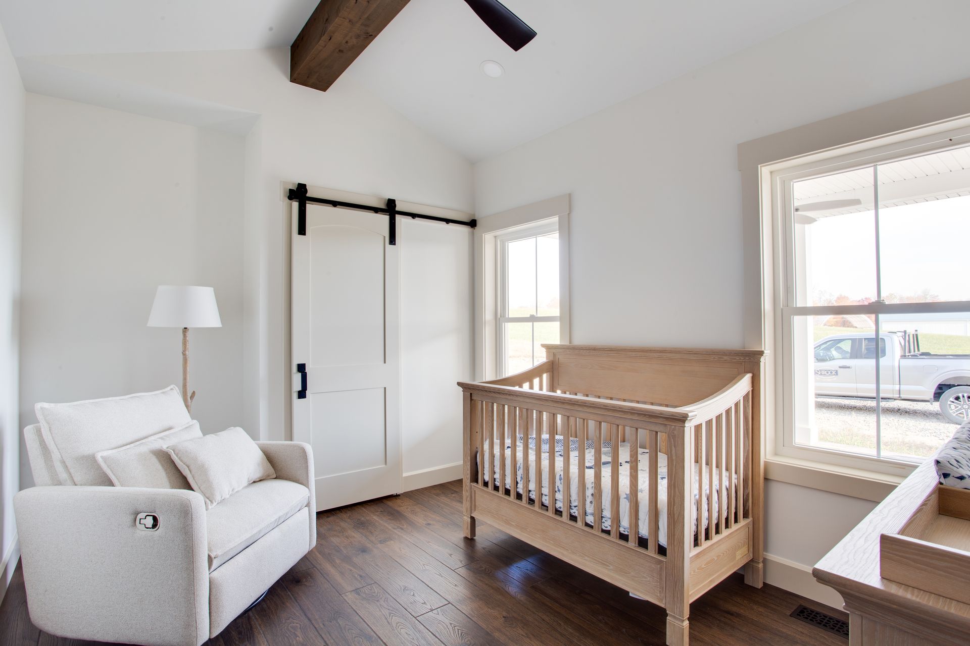 A nursery with a crib, chair, lamp and window.