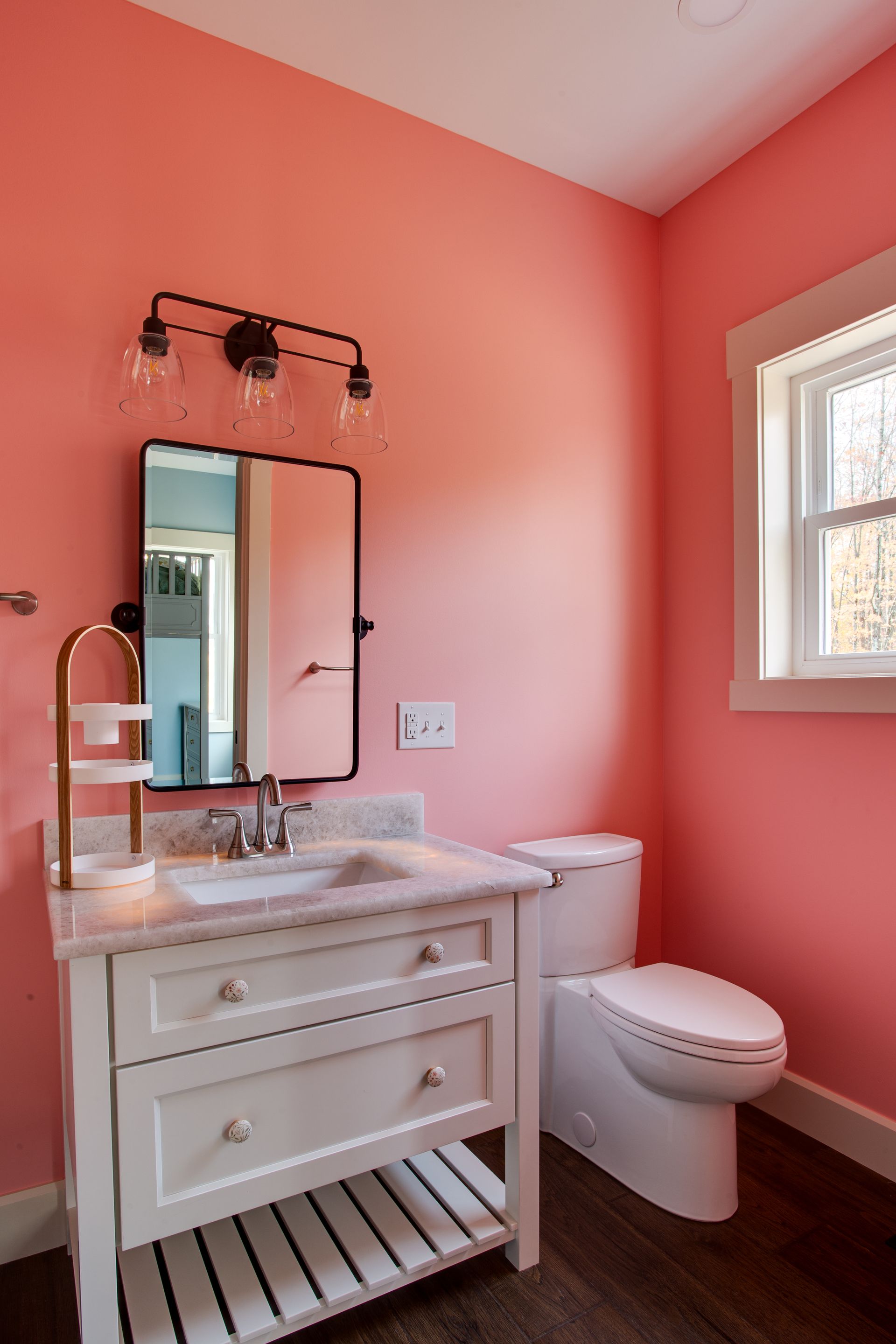 A bathroom with pink walls, a sink, toilet and mirror.