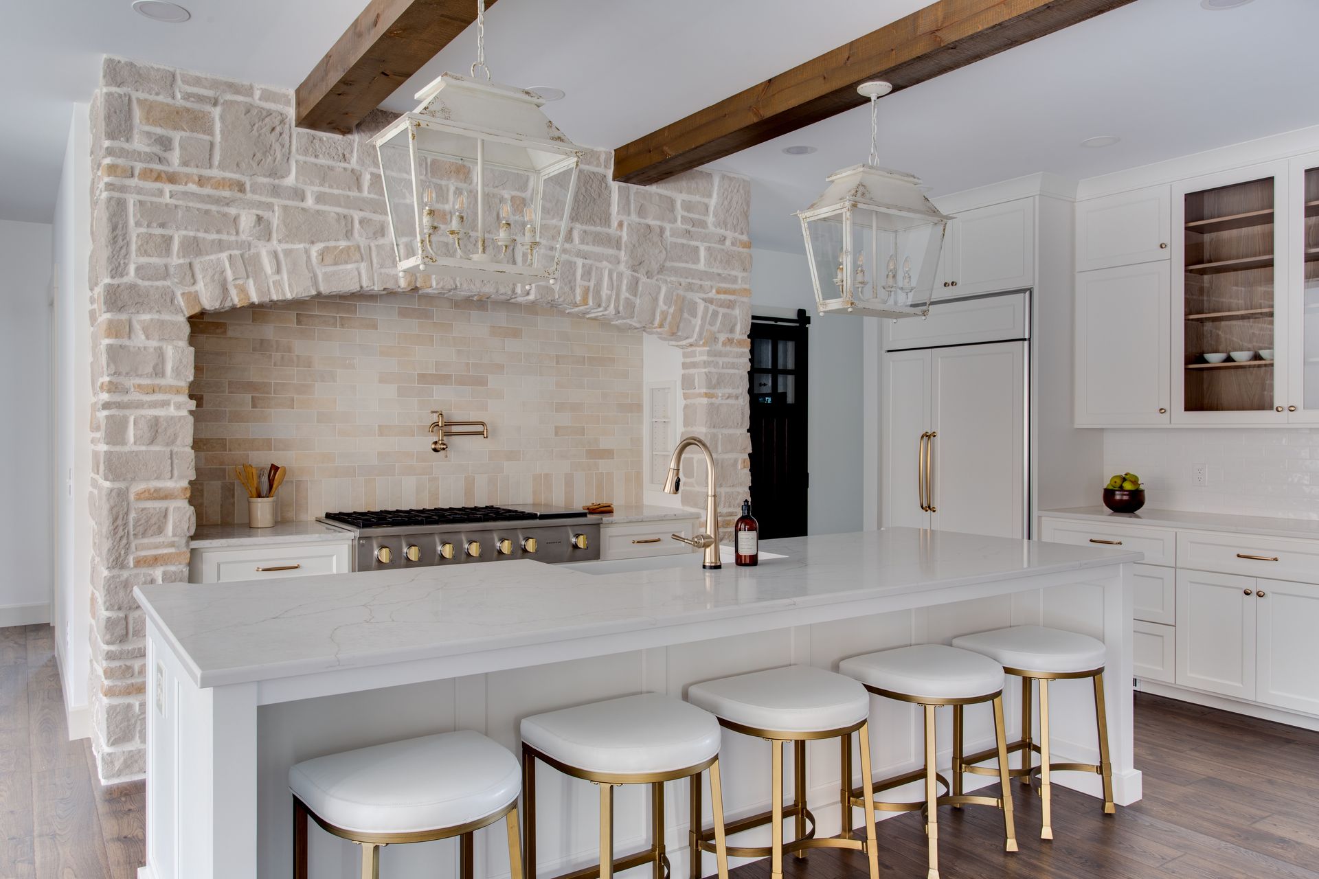 A kitchen with a large island, stools, a stove and a refrigerator.