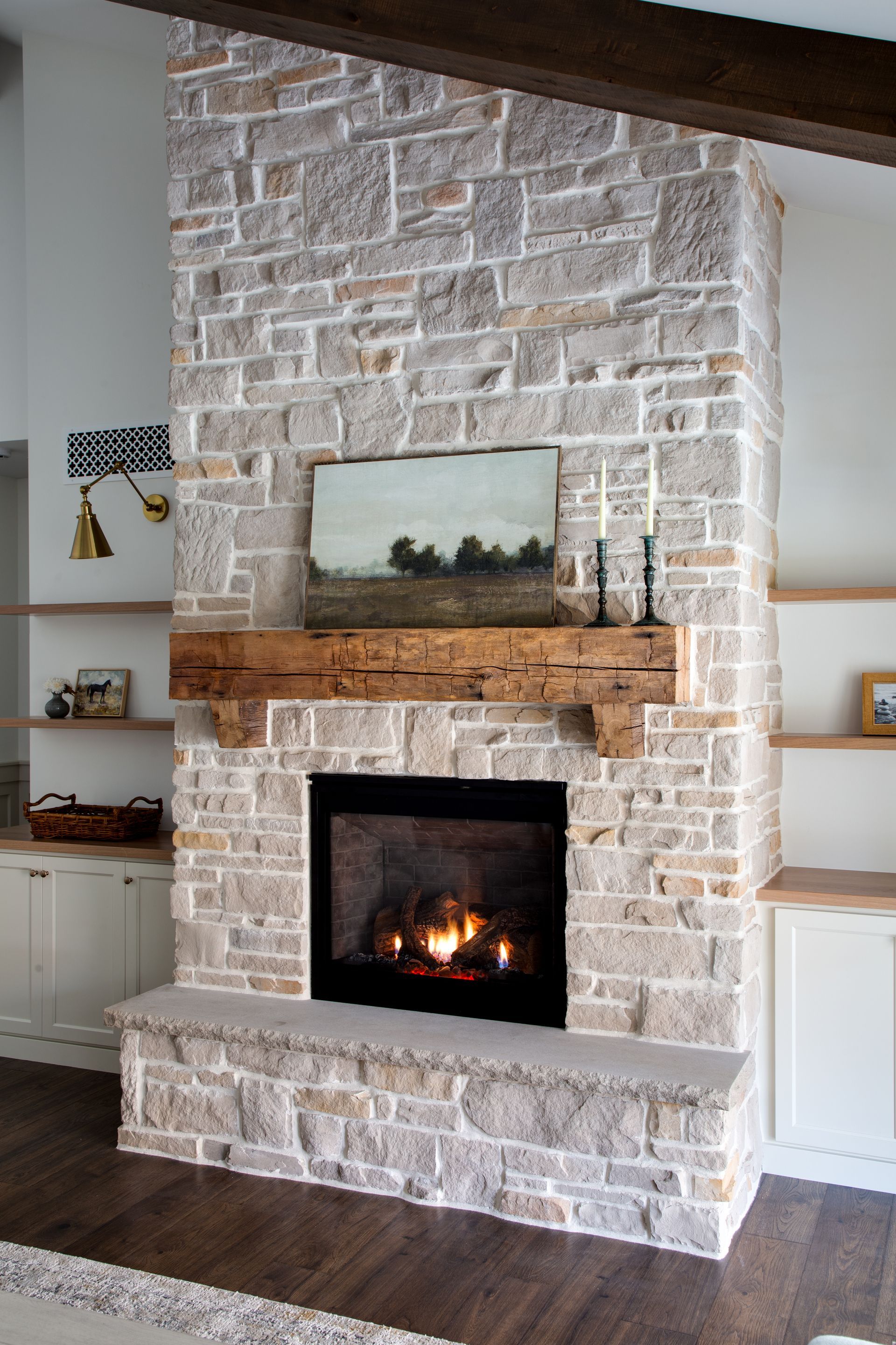 A living room with a brick fireplace and a painting on the mantle.