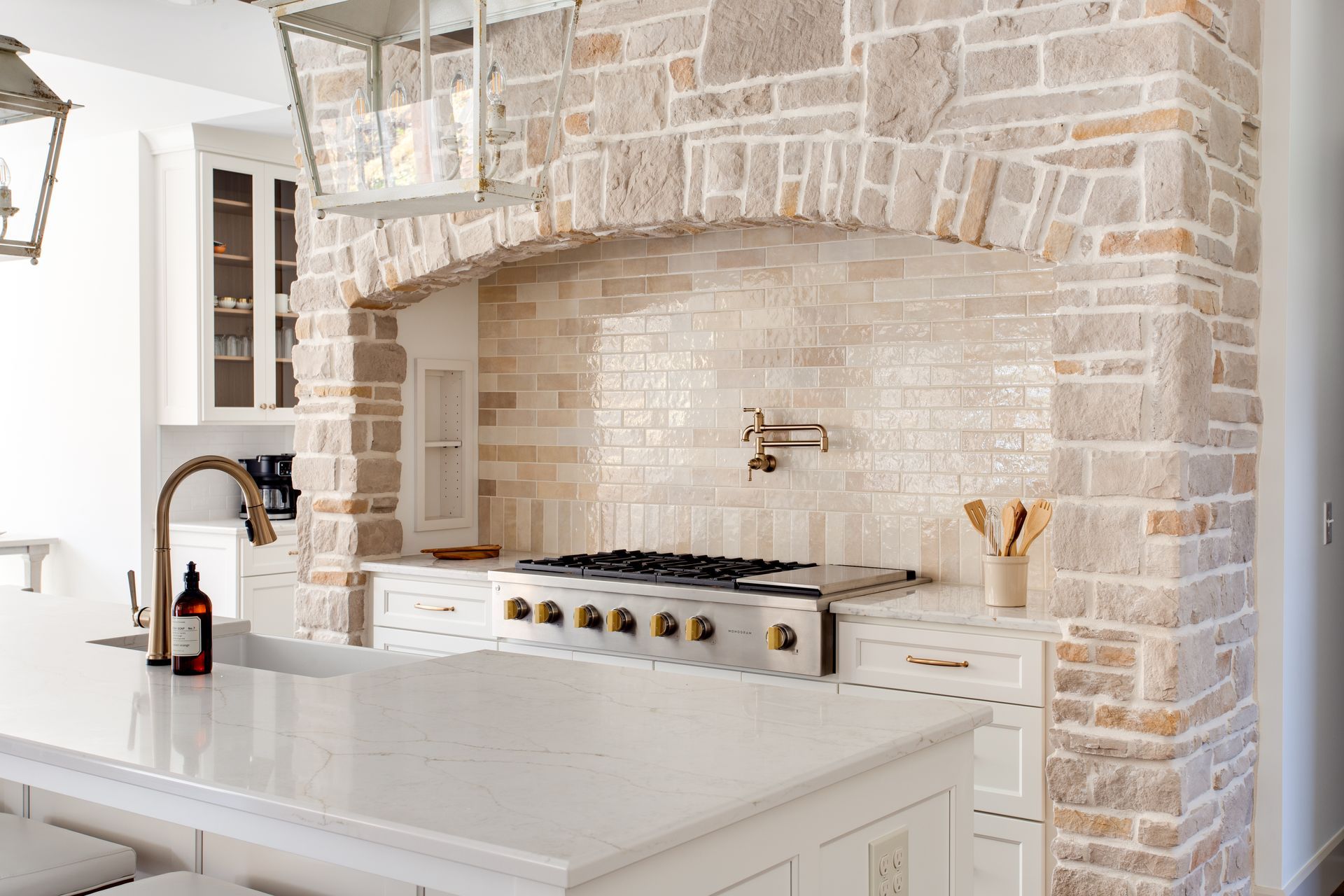 A kitchen with a stove, sink, and brick wall.
